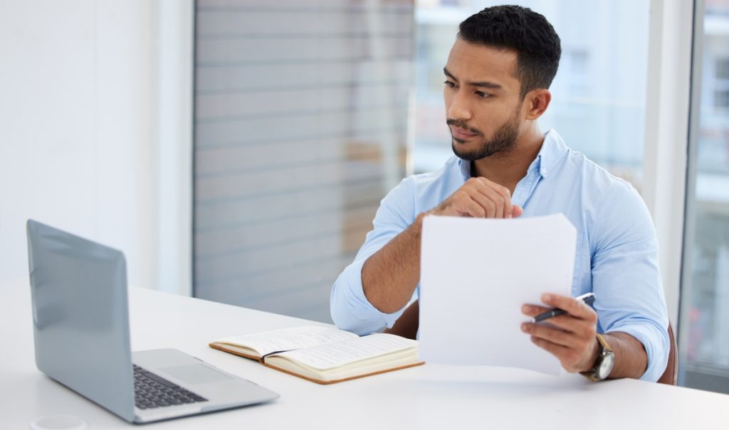 Business man holding documents and looking at a laptop