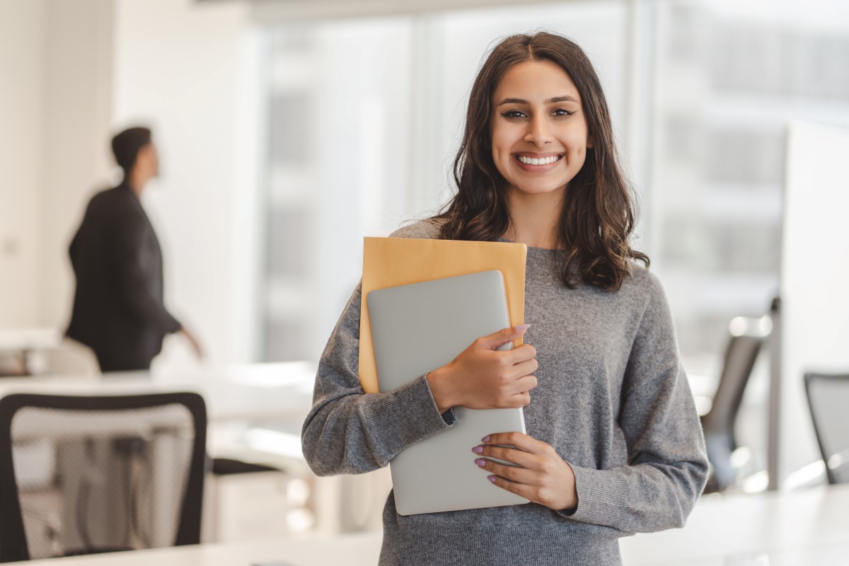 A woman holding documents and a laptop