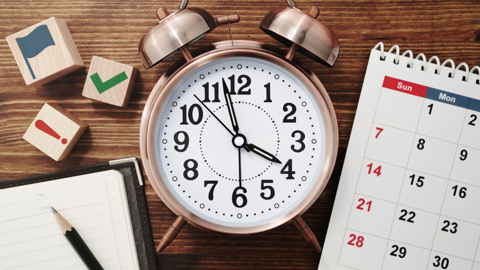 Alarm clock on a desk beside a notebook and calendar