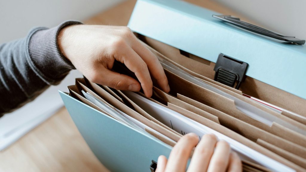 Two hands rifling through an accordion folder with paperwork in it.