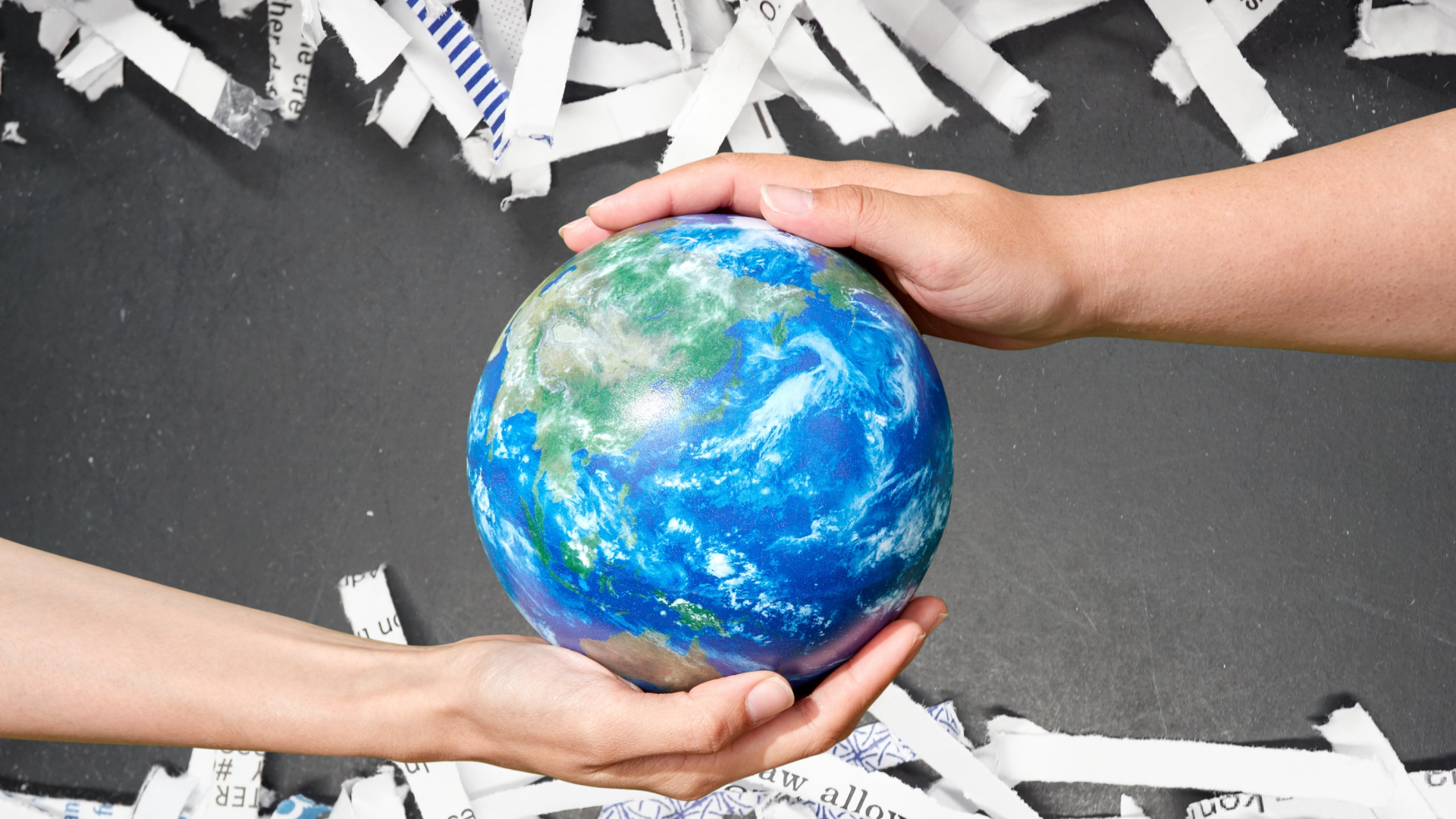 Two palms holding a globe in front of shredded pieces of paper