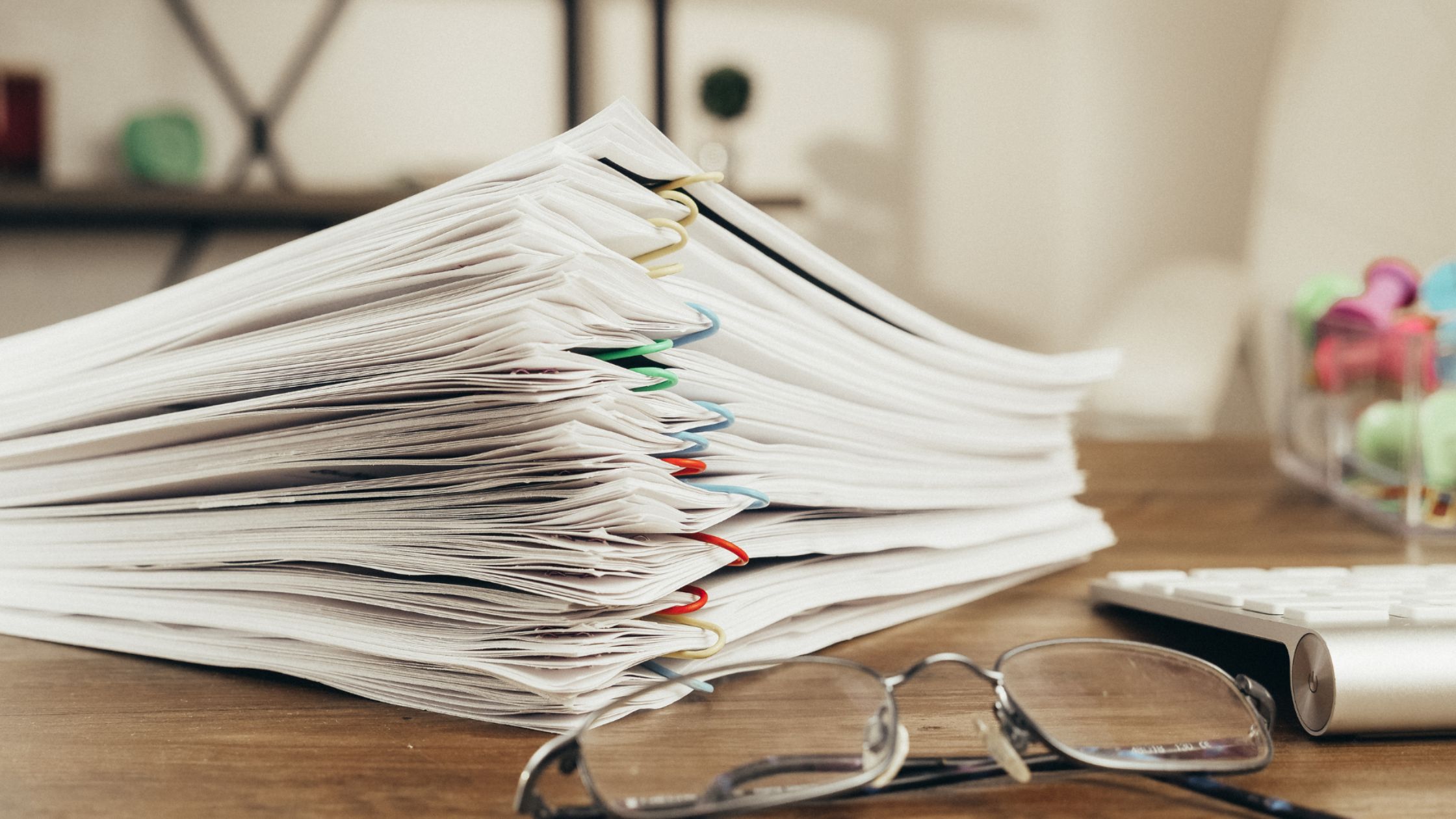 Stack of paper documents organized with binder clips on an office desk, representing business records management and document storage.