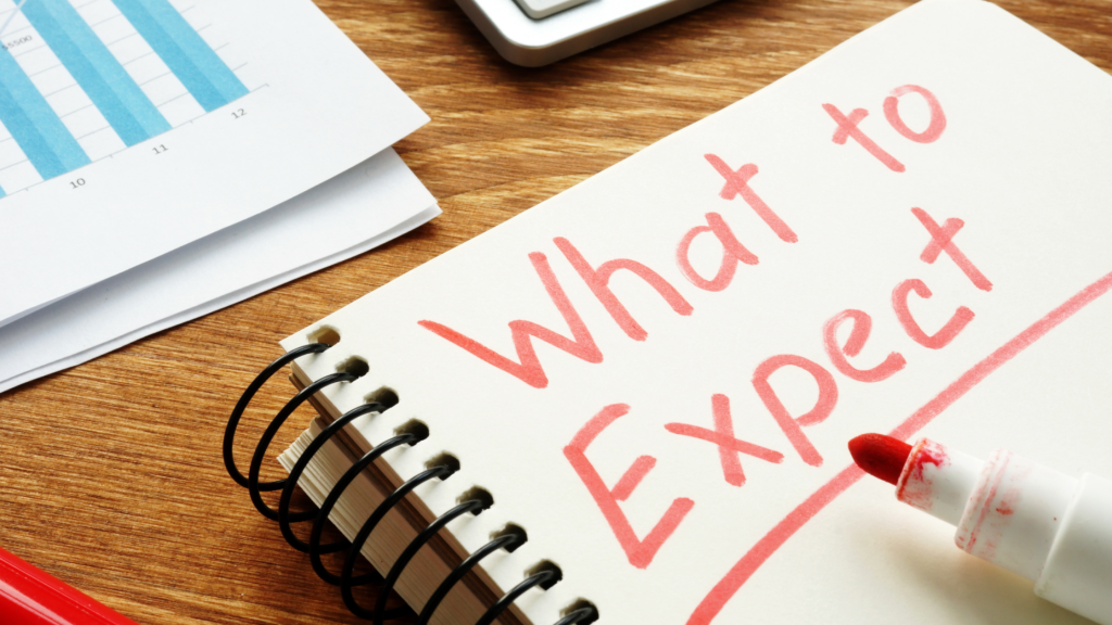 Notebook with “What to Expect” written in red marker beside business charts and paperwork on a desk.